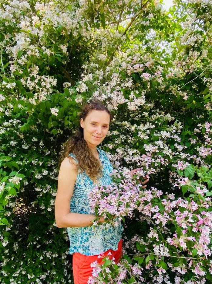 Anna of DreamAnna Gardens standing beside a flowering shrub